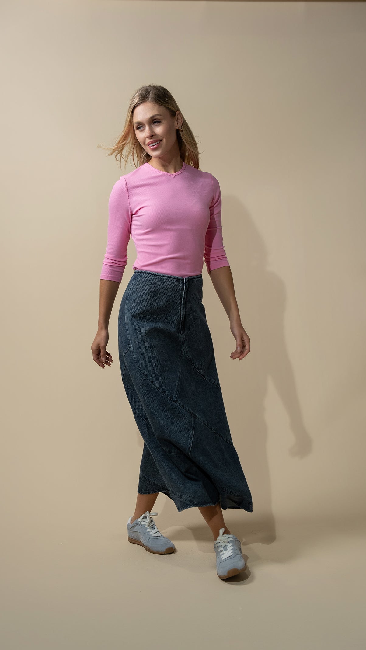 Woman wearing a pink top and dark blue pants against a beige background
